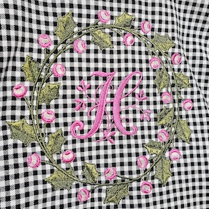 May include: Black and white gingham fabric with an embroidered wreath of green leaves and pink flowers. A large pink letter "K" is centered within the wreath, creating a personalized design.