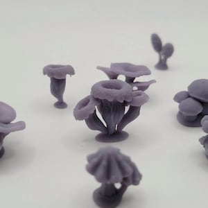 May include: Several small, purple, mushroom-shaped figurines are scattered across a white surface. The figurines vary in size and shape, with some featuring multiple caps and others a single, rounded top. The color is a muted, lavender-like hue.