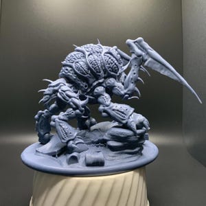 May include: A detailed grey miniature of a monstrous creature with a segmented body, multiple limbs, and a large, textured head. The figure has sharp claws and wing-like appendages, posed on a rocky base.