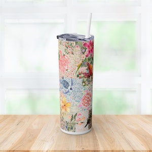 Puede incluir: Un vaso de acero inoxidable con un diseño floral y de mosaico. El vaso presenta una variedad de flores, pájaros y tortugas en tonos de rosa, azul, verde y amarillo. El vaso tiene una tapa blanca y una pajita transparente.