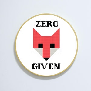 May include: A white circle with a gold border, featuring a red fox head with black eyes and a black nose. The text "ZERO GIVEN" is printed in black below the fox.