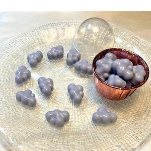 Puede incluir: Un plato de vidrio con una variedad de caramelos en forma de nube de color lavanda. Algunos caramelos están en un pequeño tazón de cobre, mientras que otros están esparcidos por el plato.