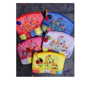 Puede incluir: Cinco pequeñas bolsas bordadas con diseños florales. Las bolsas están hechas de una tela de retazos en varios colores, incluyendo rosa, azul, amarillo y morado. Cada bolsa tiene un pequeño borla.
