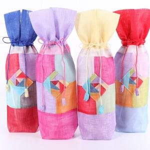 以下が含まれることがあります： 伝統的な韓国のデザインが施されたカラフルな布製のギフトバッグ4つ。バッグは柔らかく質感のある布地で作られており、巾着式になっています。バッグの色は青、ピンク、黄色、赤です。
