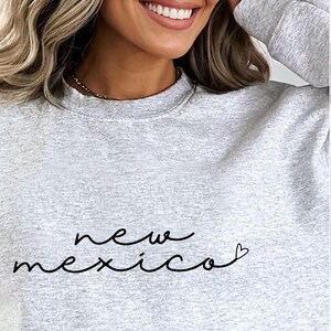 May include: A gray sweatshirt with the text "new mexico" written in black cursive with a small heart at the end of the word "mexico".