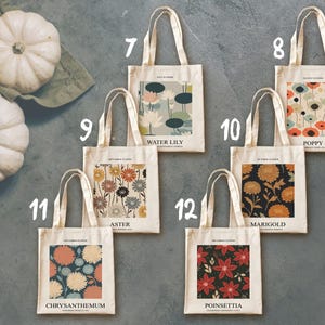 May include: A collection of cream-colored tote bags with various floral designs. Each bag features a different flower illustration, including water lilies, poppies, asters, marigolds, chrysanthemums, and poinsettias. The bags have cream-colored handles and the names of the flowers are printed on the bags.