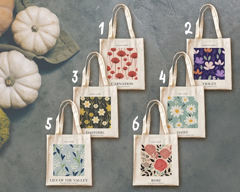 May include: Six canvas tote bags with floral designs. Each bag features a different flower: Carnation, Violet, Daffodil, Daisy, Lily of the Valley, and Rose. The bags have cream-colored fabric and long handles.