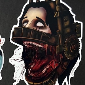 Op de afbeelding: Een sticker van een vrouwenhoofd met een metalen masker en een bloederige open mond. Het masker heeft tandwielen en pijpen. De sticker is wit met een zwarte omtrek.