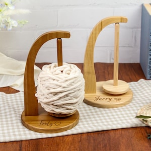 May include: Two wooden yarn holders with a white yarn ball on one and a wooden dowel on the other. The holders are personalized with the names "Emily" and "Jerry".