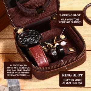 May include: A brown leather travel case with a zipper, designed to store jewelry and watches. Inside, a black watch with a red leather band, rings, and earrings are visible. The case has slots for rings and earrings, and can also hold watches.