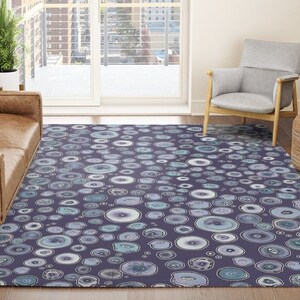 May include: A purple area rug with a repeating pattern of light blue and white circles. The rug is in a living room setting with a brown leather sofa and a gray armchair.