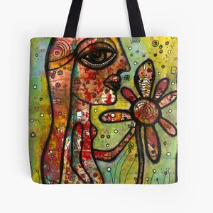 Peut inclure: Un sac fourre-tout color&eacute; avec une peinture d'une personne avec un grand &oelig;il et une fleur. La personne est peinte dans des tons de rouge, orange et jaune, tandis que la fleur est rouge et jaune. L'arri&egrave;re-plan est un m&eacute;lange de vert, jaune et blanc.