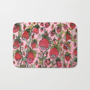 Puede incluir: Una alfombra de ba&ntilde;o rosa con un patr&oacute;n caprichoso de fresas con ojos y caras. Las fresas son rojas y verdes y est&aacute;n dispuestas en un patr&oacute;n aleatorio.