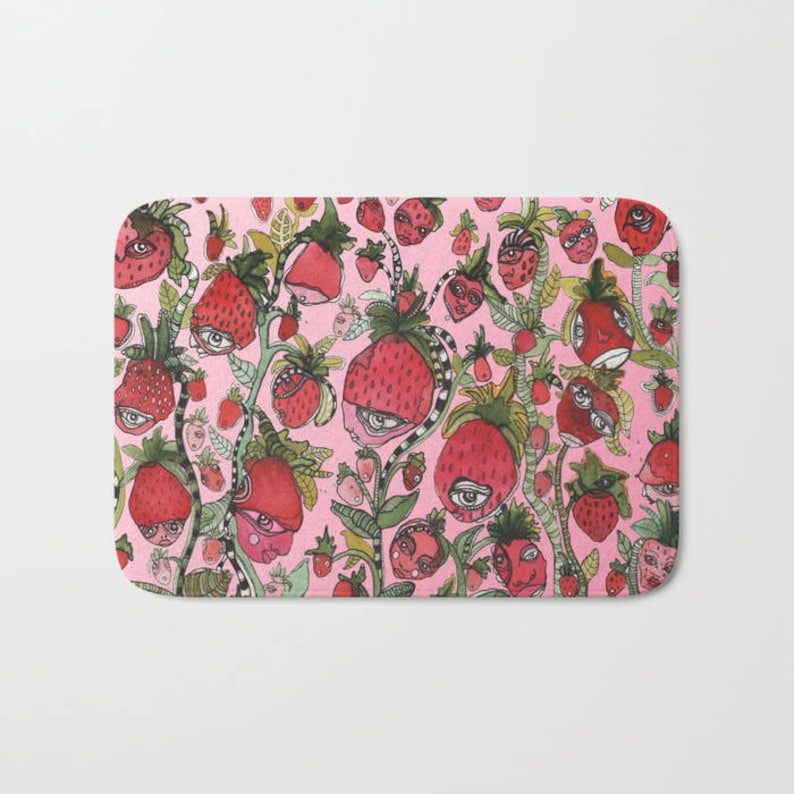 Puede incluir: Una alfombra de ba&ntilde;o rosa con un patr&oacute;n caprichoso de fresas con ojos y caras. Las fresas son rojas y verdes y est&aacute;n dispuestas en un patr&oacute;n aleatorio.