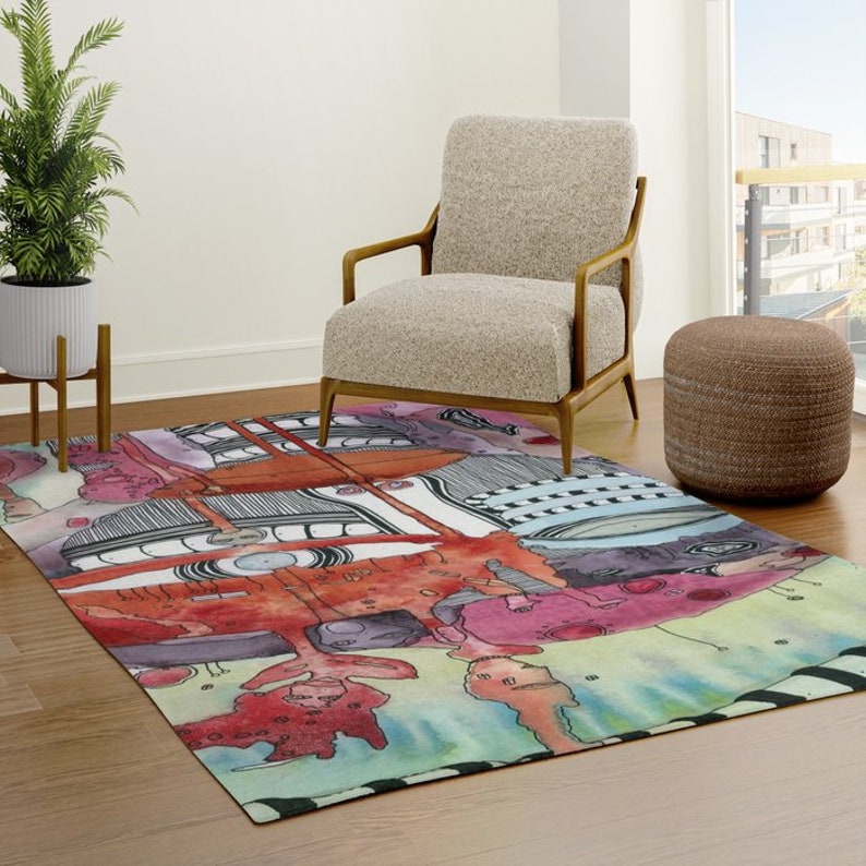May include: Abstract area rug with a colorful, geometric design featuring red, orange, pink, blue, green, and black. The rug is on a wooden floor with a chair and ottoman in the background.