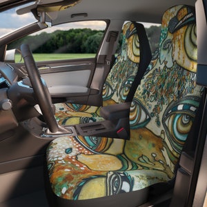 May include: A pair of car seat covers with a colorful abstract design featuring multiple eyes and a yellow, green, and blue color scheme.