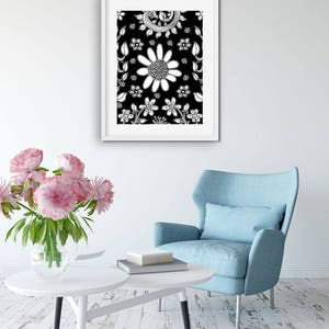 Puede incluir: Una impresi&oacute;n enmarcada en blanco y negro de un patr&oacute;n floral con flores y hojas blancas sobre un fondo negro. La impresi&oacute;n est&aacute; colgada en una pared blanca sobre un sill&oacute;n azul y una mesa de caf&eacute; blanca.