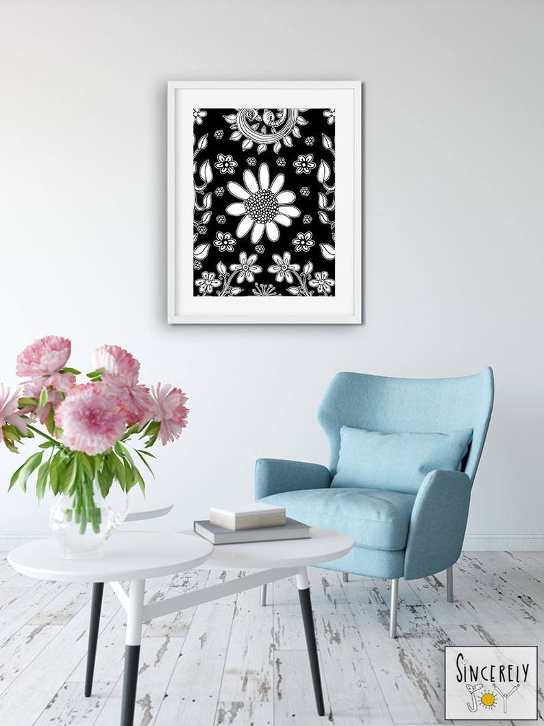 Puede incluir: Una impresi&oacute;n enmarcada en blanco y negro de un patr&oacute;n floral con flores y hojas blancas sobre un fondo negro. La impresi&oacute;n est&aacute; colgada en una pared blanca sobre un sill&oacute;n azul y una mesa de caf&eacute; blanca.