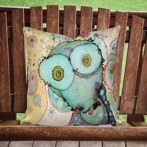 May include: A decorative pillow with a whimsical design featuring abstract shapes, swirls, and eyes in shades of blue, green, yellow, and pink on a cream background.