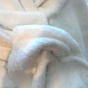 May include: Close-up of a white plush fabric with a soft, fuzzy texture. The fabric is folded and draped, showing the texture and softness.