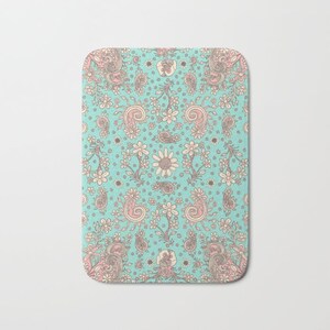 May include: A turquoise blue bath mat with a pink and white paisley pattern. The pattern features floral designs and paisley shapes.