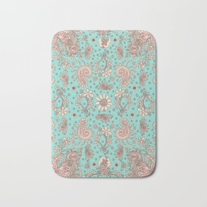 May include: A turquoise blue bath mat with a pink and white paisley pattern. The pattern features floral designs and paisley shapes.