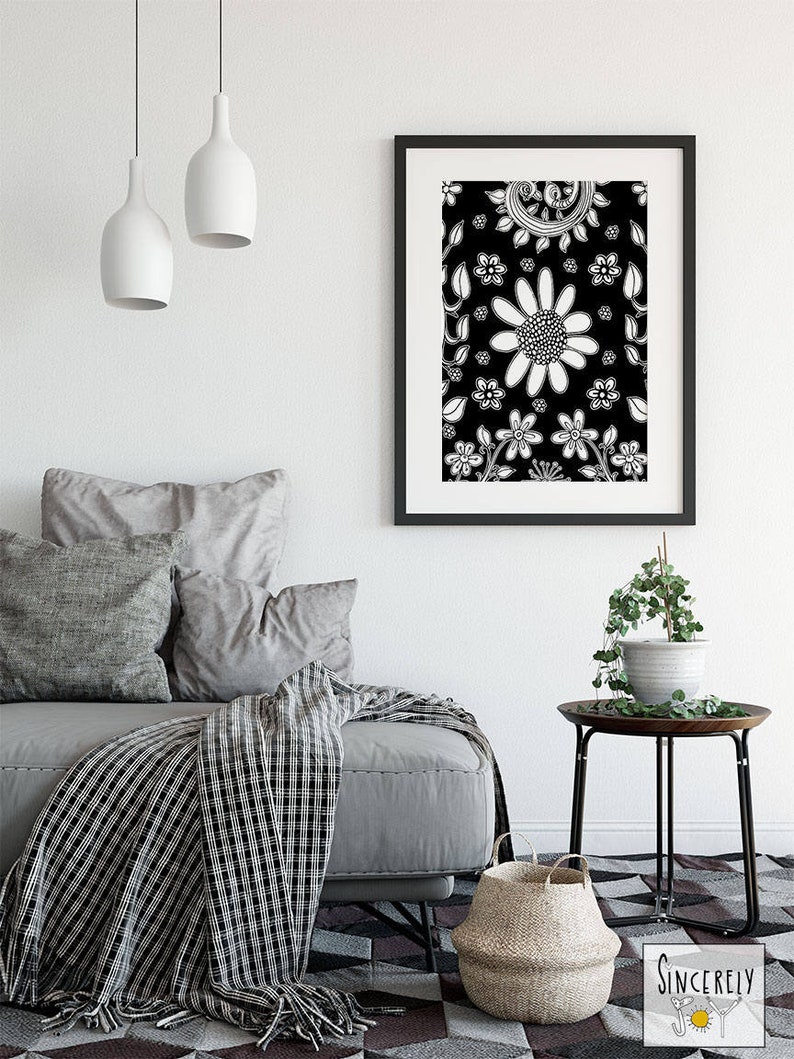 Puede incluir: Impresi&oacute;n de arte floral en blanco y negro en un marco negro colgado en una pared blanca sobre un sof&aacute; gris con almohadas y una manta de color blanco y negro. Una peque&ntilde;a mesa auxiliar negra con una planta en maceta se encuentra junto al sof&aacute;.