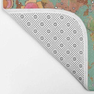 May include: A white bath mat with a black dot pattern. The mat has a teal, pink, and brown floral design with a white border.