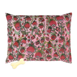 May include: Pink dog bed with a strawberry print featuring strawberries with eyes. The bed comes with a bone-shaped toy.