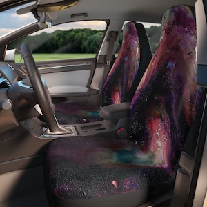 May include: Two car seat covers with a galaxy print. The print features shades of purple, pink, blue, and white.