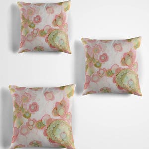 May include: Three decorative throw pillows with a pink and green abstract pattern. The pillows are on a white background.