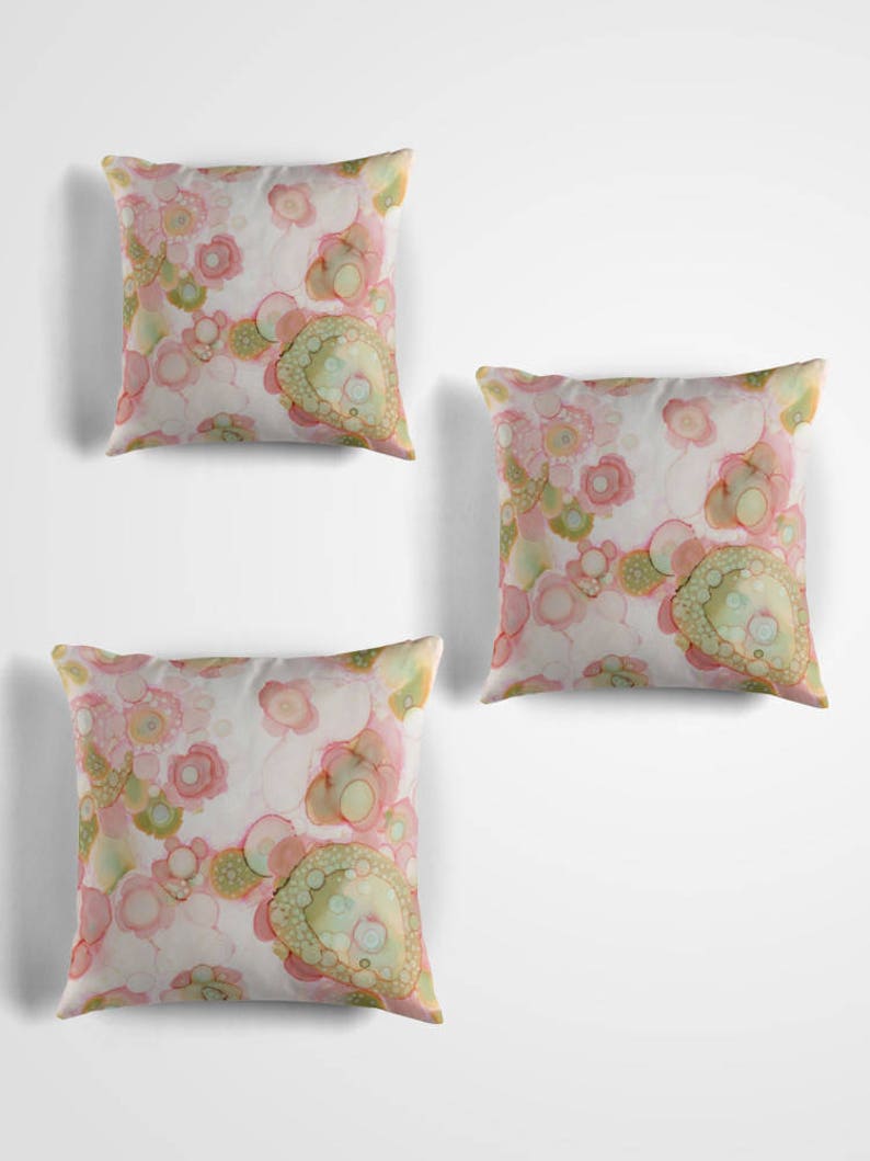 May include: Three decorative throw pillows with a pink and green abstract pattern. The pillows are on a white background.