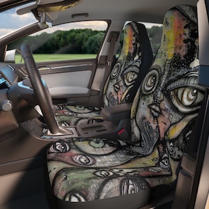 May include: A pair of car seat covers with a colorful abstract design featuring eyes and faces. The design is reminiscent of graffiti art.
