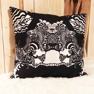 May include: Black and white decorative pillow with an intricate design featuring a stylized face. The pillow is made of fabric and has a square shape.