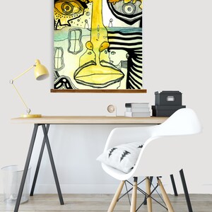 May include: Abstract art print featuring a yellow, green, and black face with a striped pattern. The print is hanging on a wall above a desk with a white chair and a lamp.