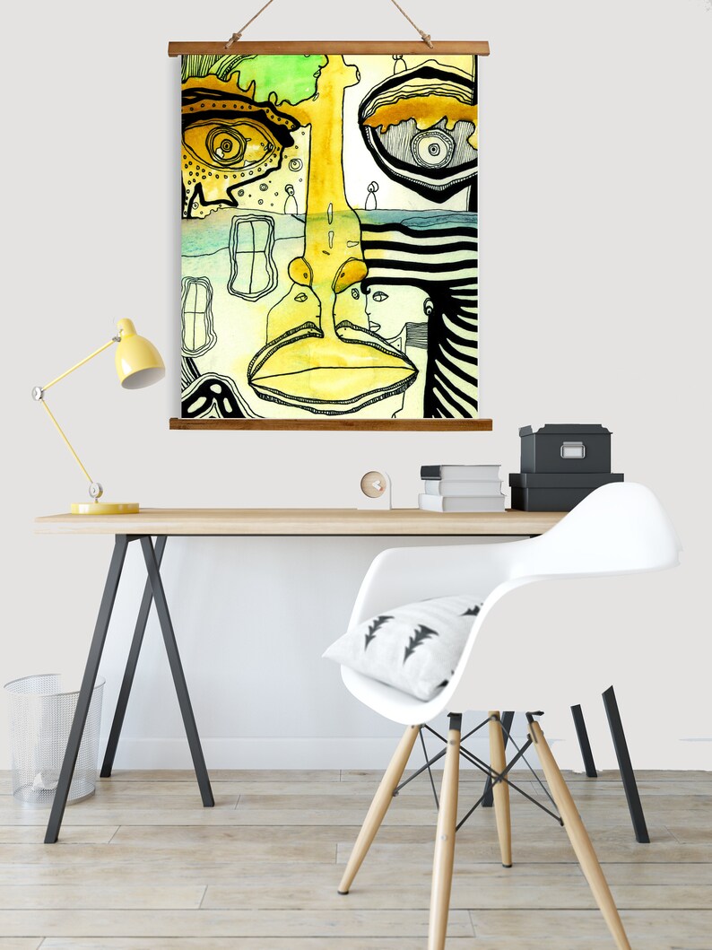 May include: Abstract art print featuring a yellow, green, and black face with a striped pattern. The print is hanging on a wall above a desk with a white chair and a lamp.