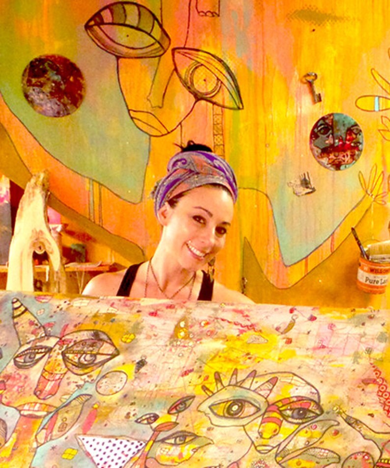 May include: A woman with a colorful headscarf is working on a large canvas painting. The canvas is covered in colorful abstract faces and patterns. The woman is smiling and appears to be enjoying her work.