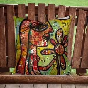 May include: A colorful throw pillow with an abstract design featuring a face and a flower. The pillow is made of fabric and has a textured surface.
