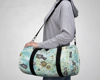 Puede incluir: Una bolsa de lona azul y verde con una correa negra y un patrón abstracto blanco y dorado. La bolsa la lleva una persona.