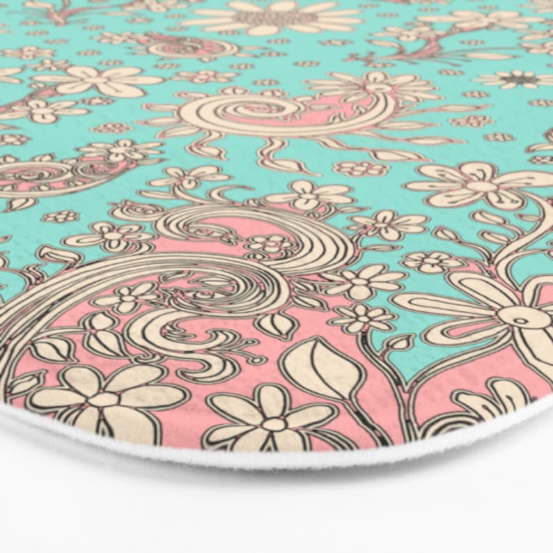 May include: A teal and pink patterned bath mat with a floral design. The pattern features swirls, leaves, and flowers.