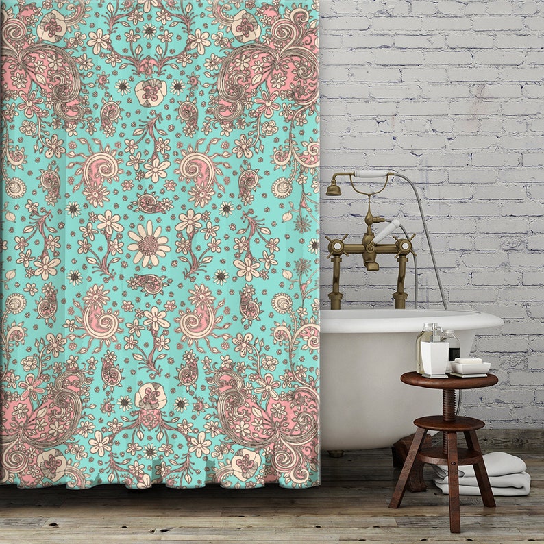 May include: A turquoise shower curtain with a pink and cream paisley pattern. The shower curtain is hanging in a bathroom with a white brick wall and a white bathtub.