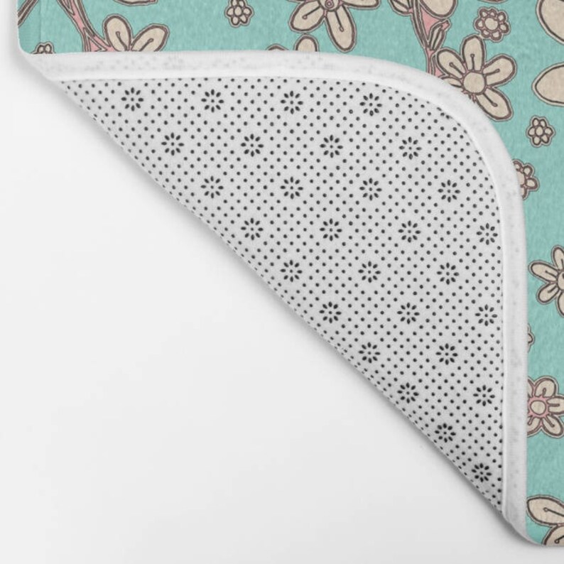 May include: A turquoise blue bath mat with a white background and a pattern of pink and white flowers. The mat has a white non-slip backing with small black dots.