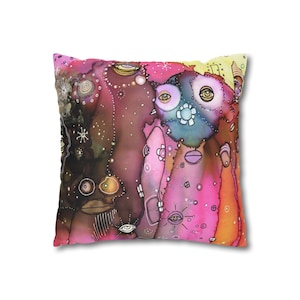 May include: Square decorative pillow with an abstract design. The artwork features a whimsical composition of faces and shapes in shades of pink, purple, brown, and blue. The design includes eye-like shapes and floral elements, creating a unique and artistic aesthetic.