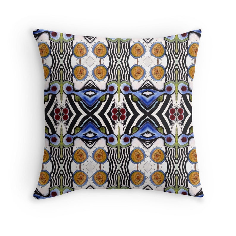 Puede incluir: Una almohada blanca con un patr&oacute;n geom&eacute;trico colorido. El patr&oacute;n presenta rayas blancas y negras, remolinos azules y verdes y c&iacute;rculos amarillos y naranjas.