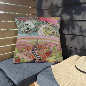 May include: A colorful throw pillow with a whimsical design featuring a landscape with hills, waves, and strawberries. The pillow is made of fabric and has a square shape.
