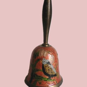 Pu&ograve; includere: Una campana decorativa con un manico in bronzo e un corpo a forma di campana rosso. La campana presenta un disegno dipinto di un uccello appollaiato su un ramo con foglie verdi. La campana ha un bordo in bronzo.
