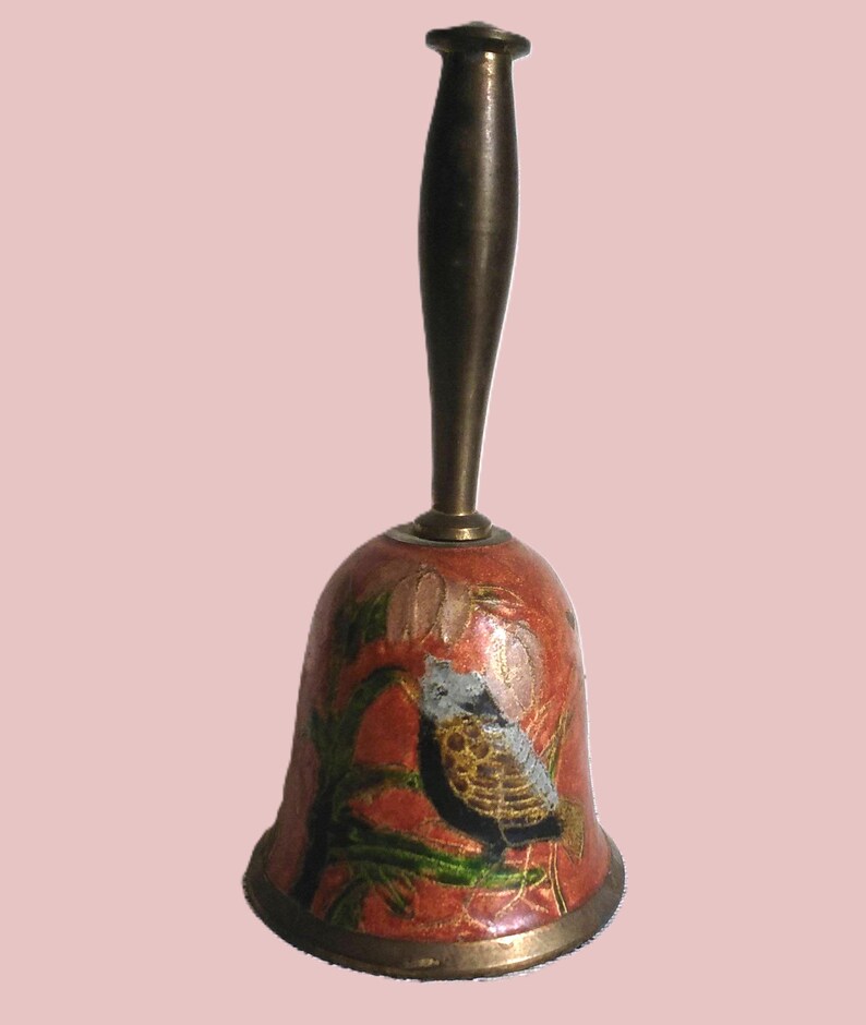 Pu&ograve; includere: Una campana decorativa con un manico in bronzo e un corpo a forma di campana rosso. La campana presenta un disegno dipinto di un uccello appollaiato su un ramo con foglie verdi. La campana ha un bordo in bronzo.