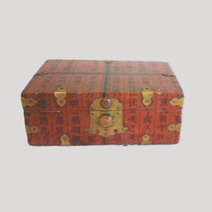 May include: A rectangular wooden box with a reddish-brown finish, featuring black Chinese calligraphy characters across the surface. The box is accented with decorative brass corner plates, hinges, and a central brass latch with a wooden knob.