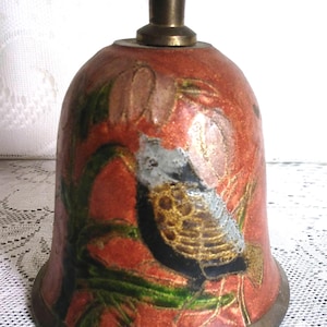 Pu&ograve; includere: Una campana decorativa con manico e base in bronzo. La campana ha uno sfondo rosso con un disegno dipinto di uccelli e fiori nei toni dell'oro, nero, verde e bianco. La campana &egrave; probabilmente in metallo.