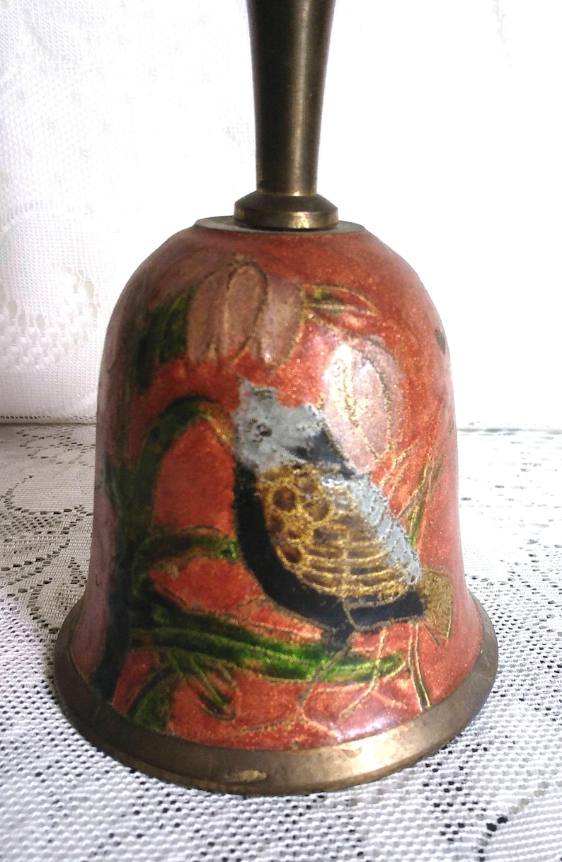 Pu&ograve; includere: Una campana decorativa con manico e base in bronzo. La campana ha uno sfondo rosso con un disegno dipinto di uccelli e fiori nei toni dell'oro, nero, verde e bianco. La campana &egrave; probabilmente in metallo.